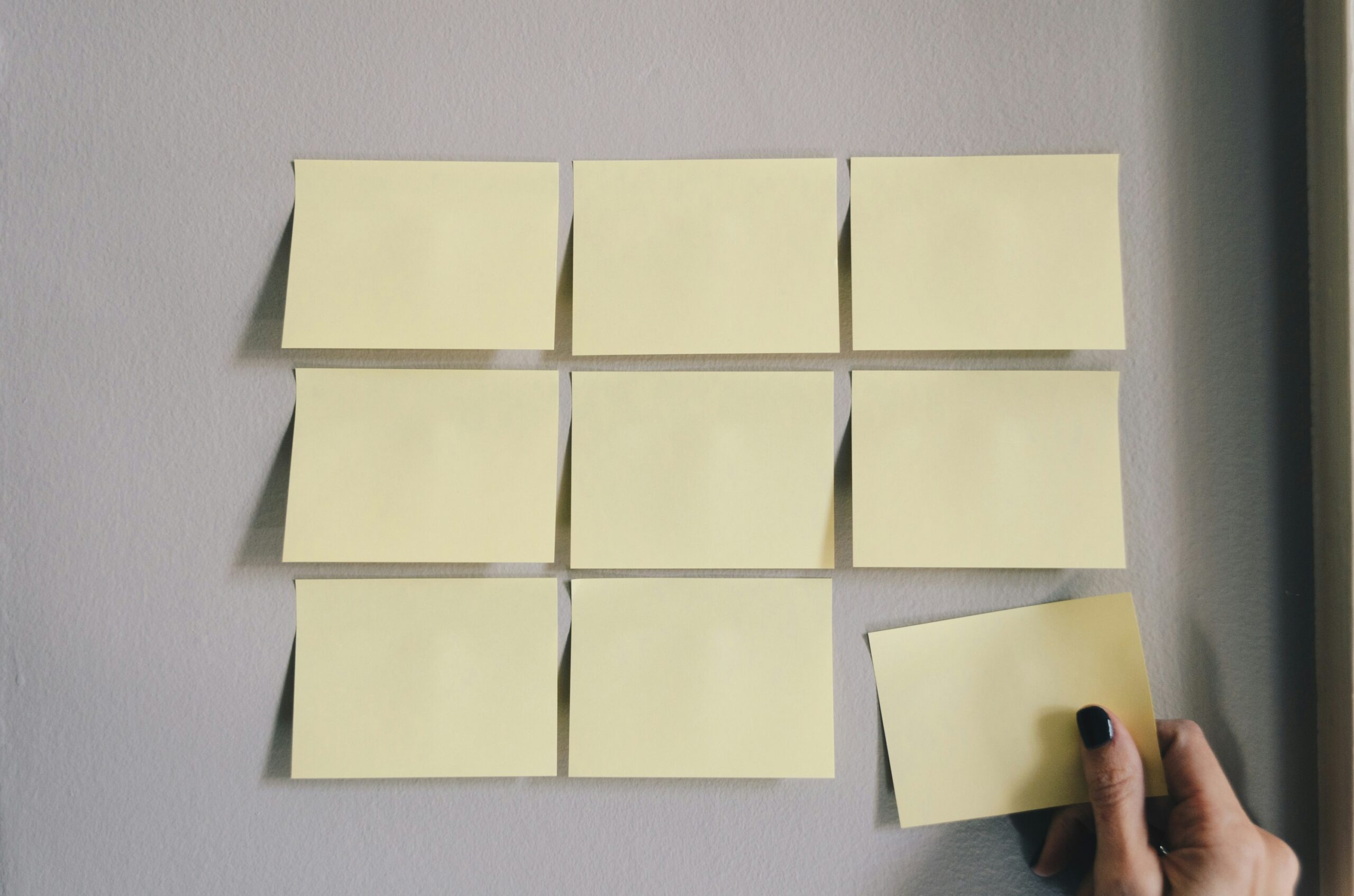 Nine yelloe sticky notes on a wall，with a hand placing another sticky note.